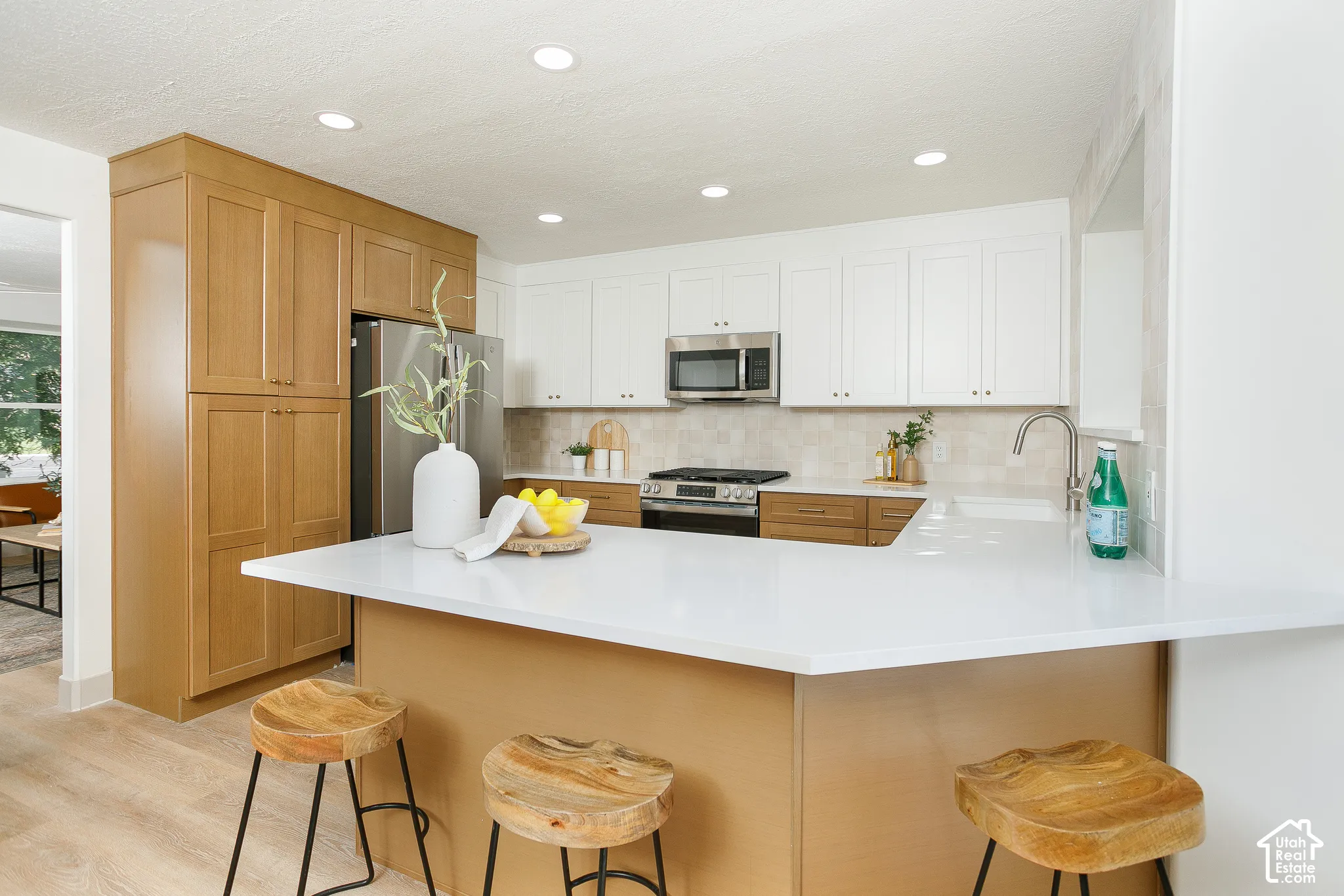 Kitchen featuring a white countertop island, stainless steel appliances, two-tone cabinetry, recessed lighting, and wood-finish flooring