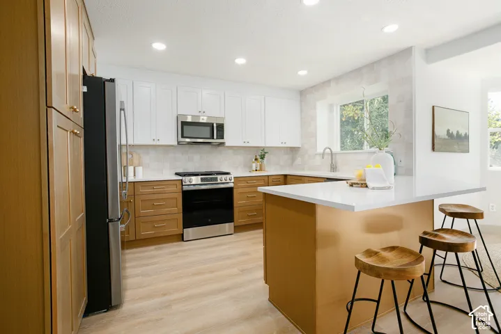 Kitchen featuring a two-tone cabinetry design, stainless steel appliances, light-toned backsplash, light wood-finish flooring, and recessed lighting