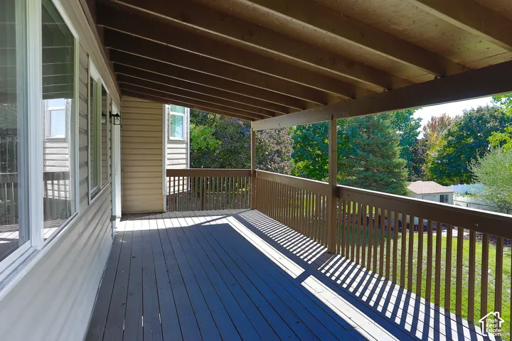 Expansive covered deck featuring a wood-finish floor and railing, exterior wall sconces, and multiple windows