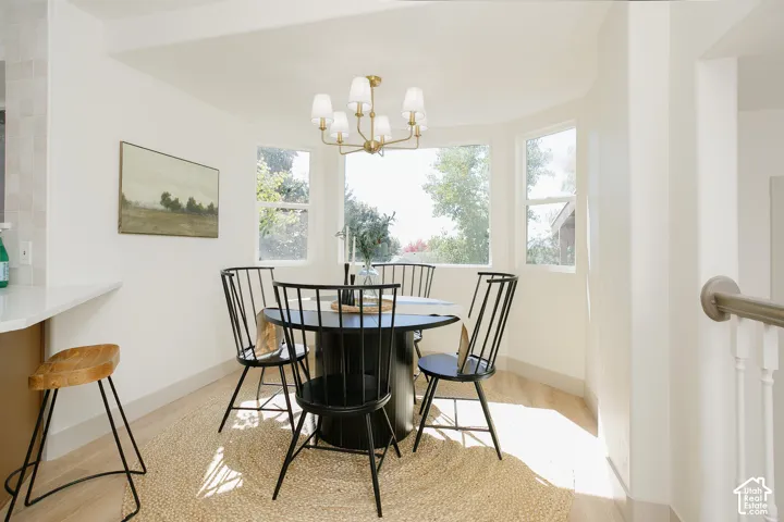 Bay window with multiple large windows, gold-tone chandelier, wood-finish flooring, and white walls