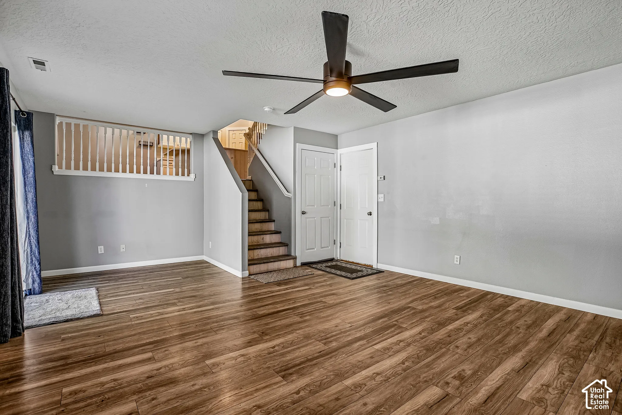 Wood-finish flooring throughout, a modern ceiling fan with integrated lighting, and a white balustrade