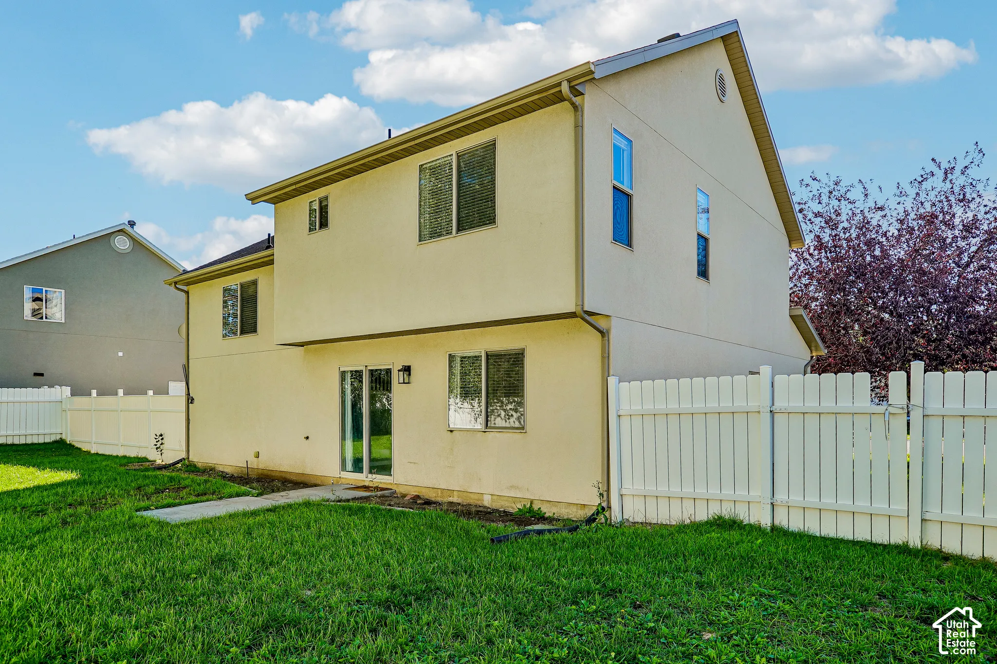Two-story exterior with a sliding glass door, multiple windows, and a white privacy fence