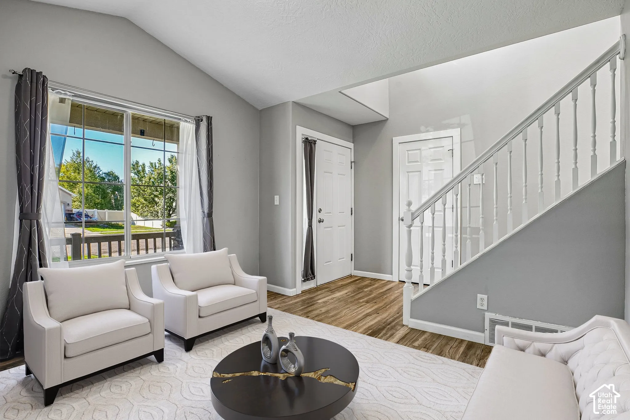 Vaulted ceiling, large window, wood-finish flooring, white staircase with balusters, and white paneled doors