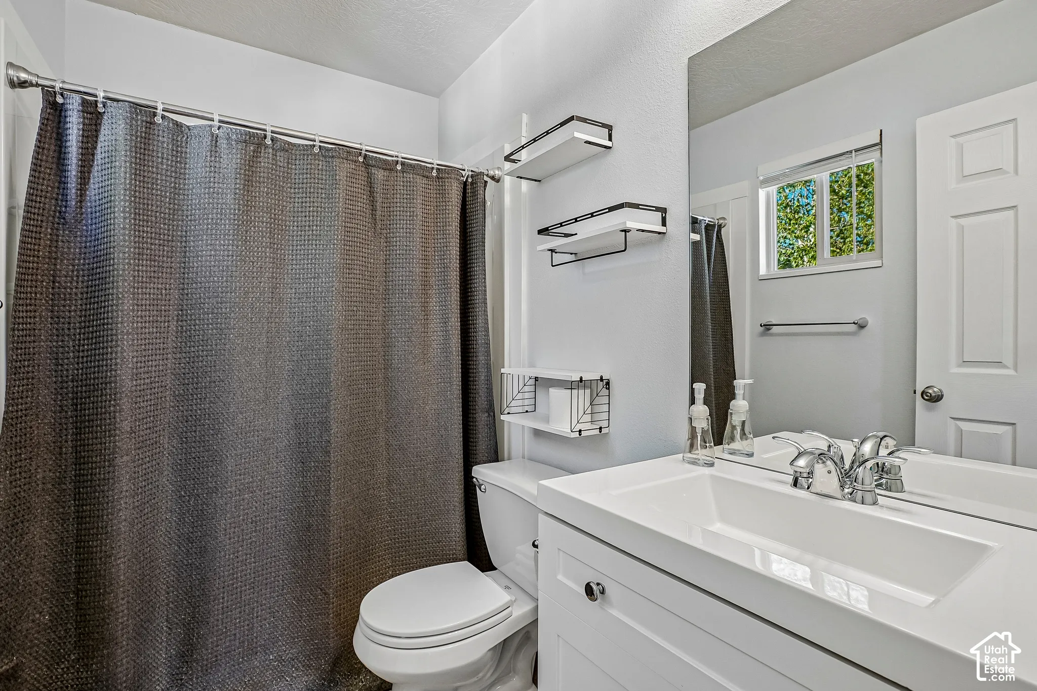 Bathroom featuring a shower with a chrome rod, a toilet, a vanity with an integrated sink, a large mirror, and a window