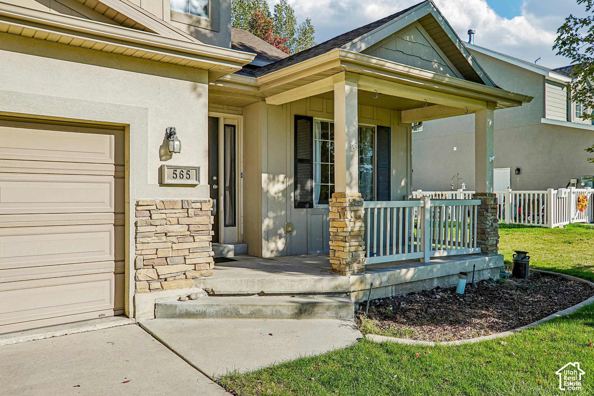 Stucco exterior with stone veneer accents, covered front porch, concrete steps, and an attached garage with a sectional door
