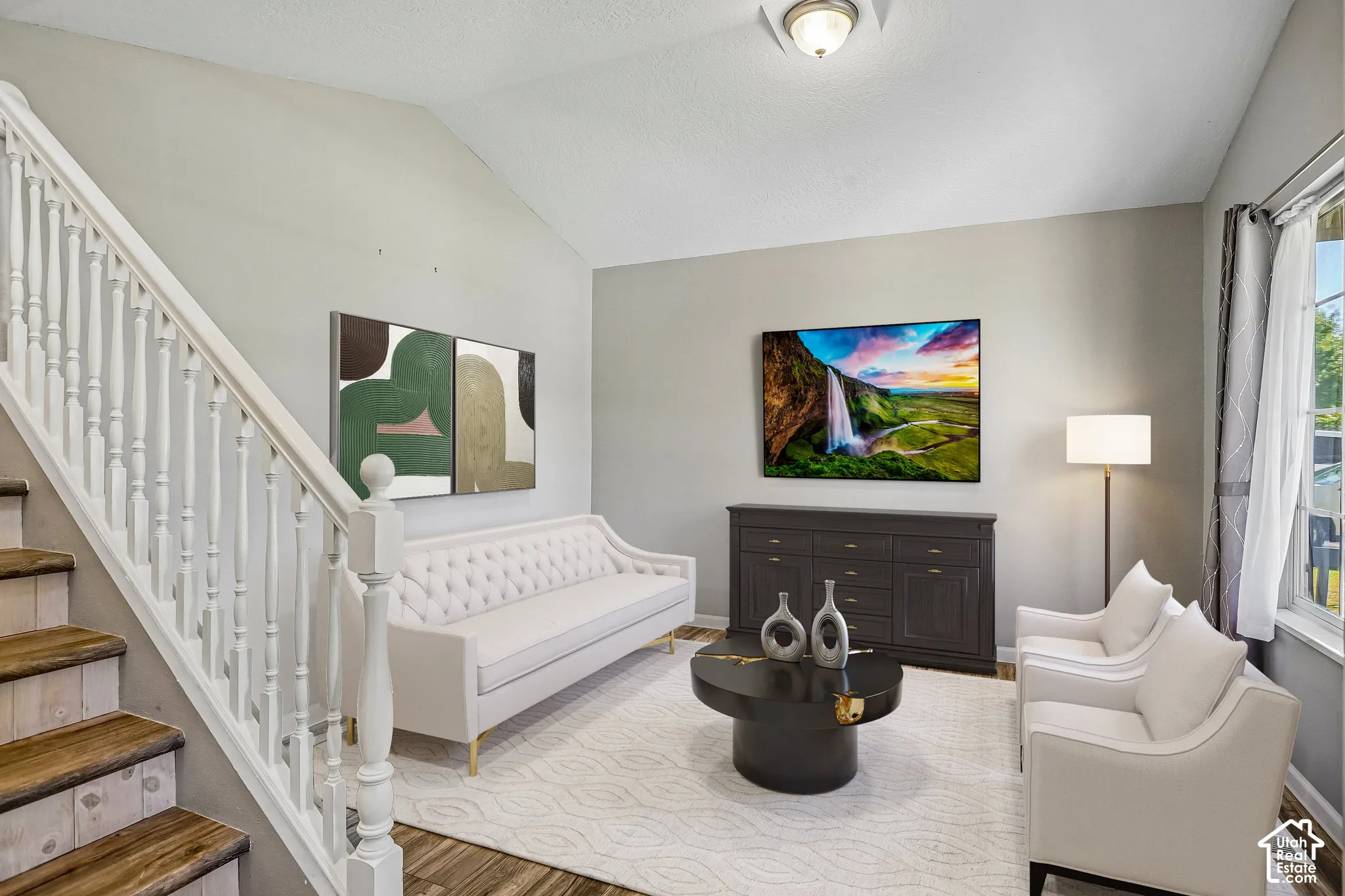 Vaulted ceiling with a flush-mount light fixture, a staircase with wood-finish treads and white balusters, and wood-finish flooring