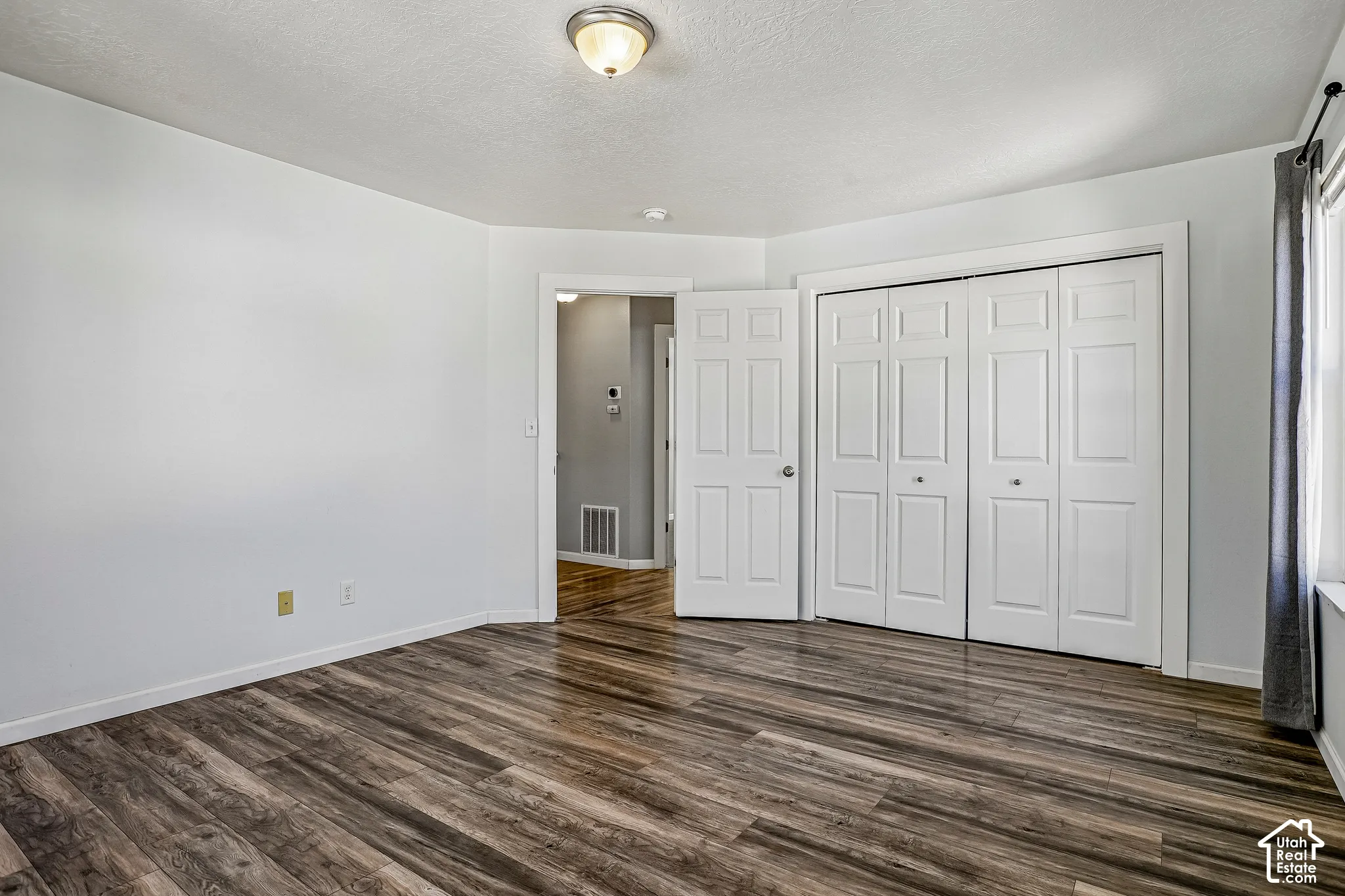 Spacious room featuring wood-finish flooring, white walls, a flush-mount ceiling light, and white paneled bi-fold closet doors