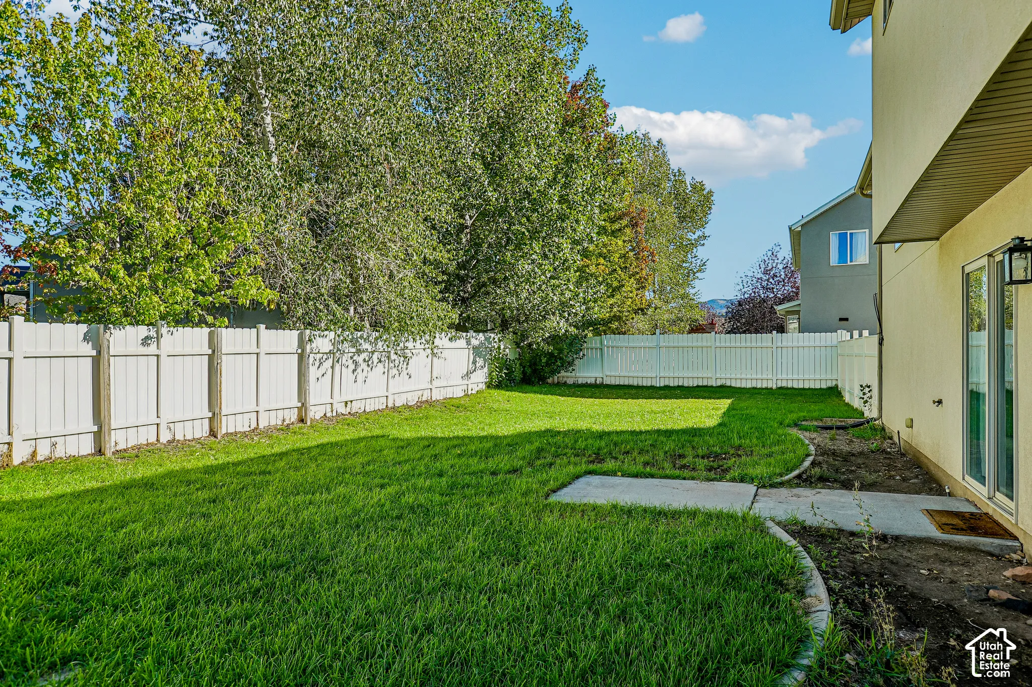 Expansive lawn area, privacy fencing, exterior wall with patio door, and concrete patio