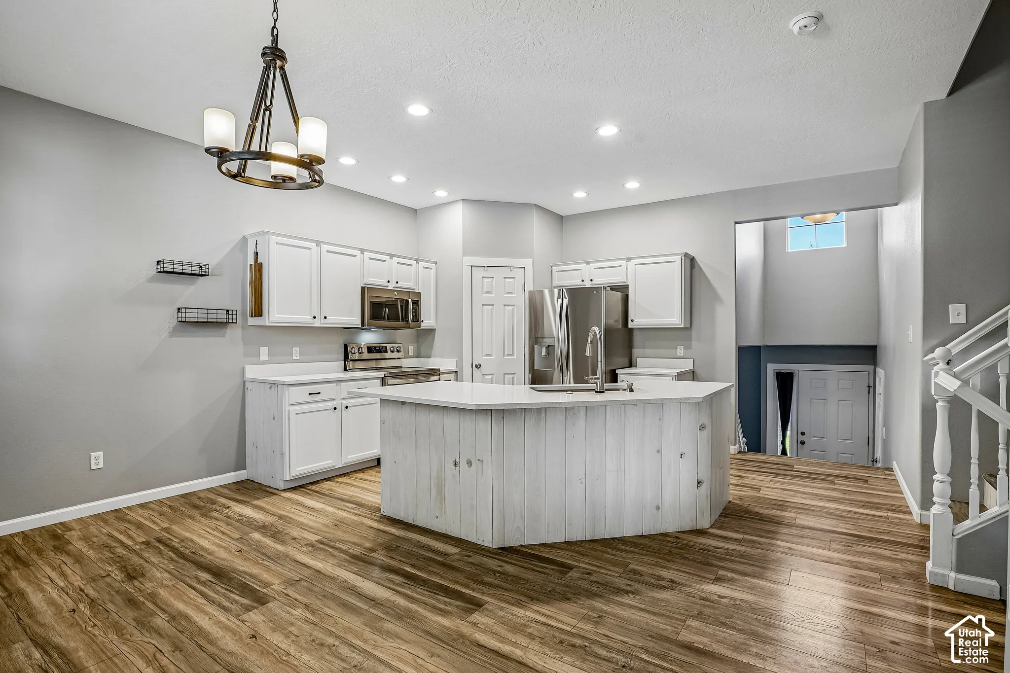 Kitchen featuring white cabinetry, stainless steel appliances, a center island with sink, wood-finish flooring, and recessed lighting