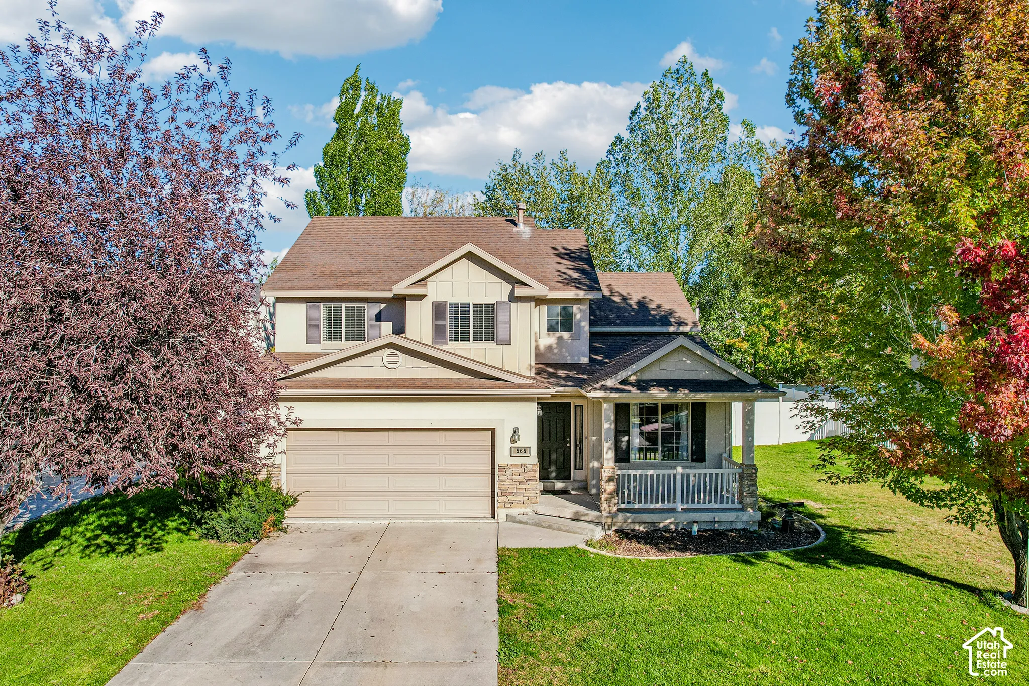 Two-story property featuring a stone and siding exterior, front porch with white railing, attached two-car garage, and a concrete driveway