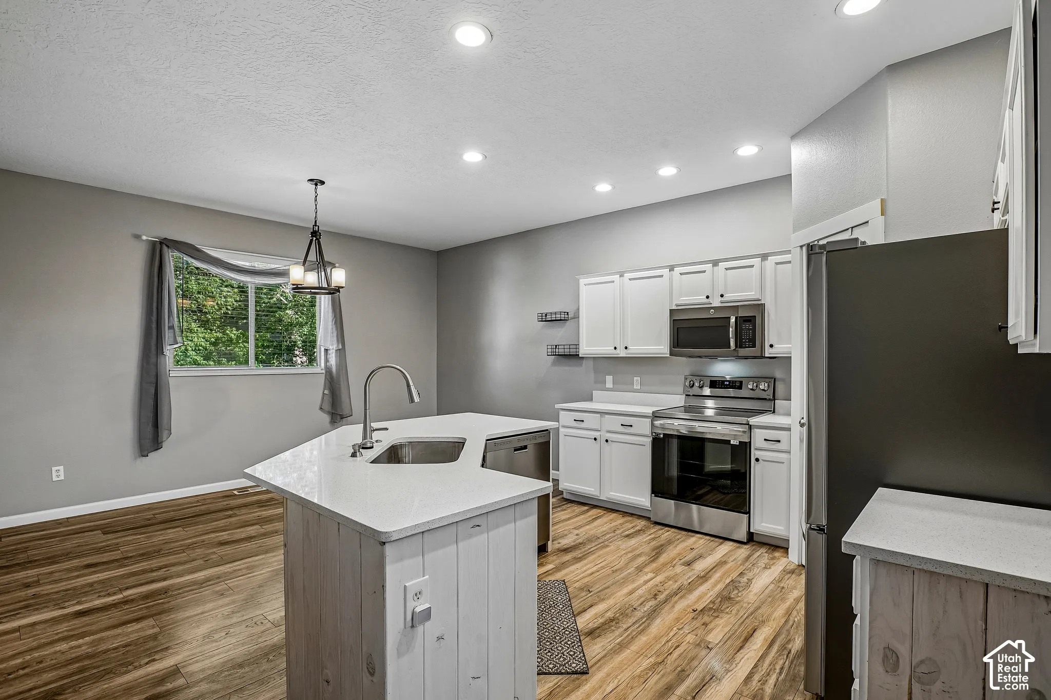 Kitchen featuring stainless steel appliances, white cabinetry, a central island with a sink, wood-finish flooring, and recessed lighting