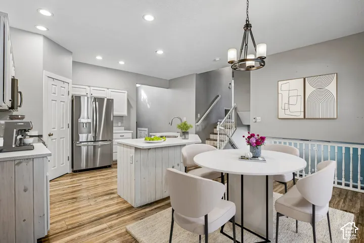 Integrated kitchen and dining area featuring wood-finish flooring, white cabinetry, and stainless steel appliances