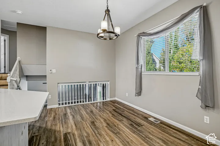 Wood-finish flooring, white window blinds, white window trim, white railing, and a bronze-finish chandelier