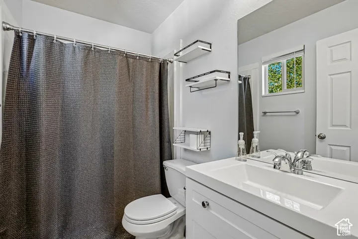 Bathroom featuring a shower with a chrome rod, a toilet, a vanity with an integrated sink, a large mirror, and a window