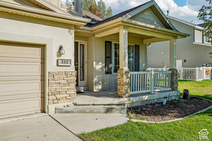 Stucco exterior with stone veneer accents, covered front porch, concrete steps, and an attached garage with a sectional door