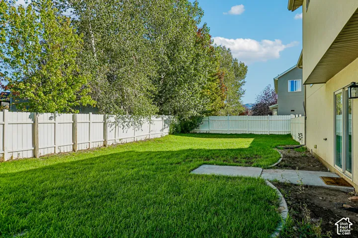 Expansive lawn area, privacy fencing, exterior wall with patio door, and concrete patio
