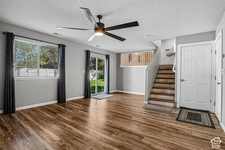 Wood-finish flooring throughout, ceiling fan with integrated lighting, glass sliding door to the exterior, multiple windows with blinds, and staircase with wood railing