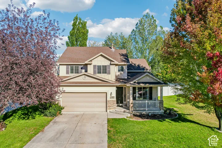 Two-story property featuring a stone and siding exterior, front porch with white railing, attached two-car garage, and a concrete driveway