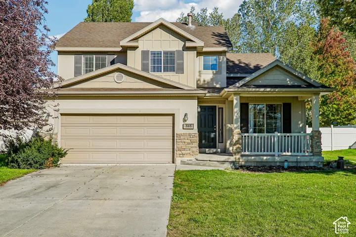 Two-story residence featuring a covered front porch, stone and siding exterior, two-car garage, and mature landscaping