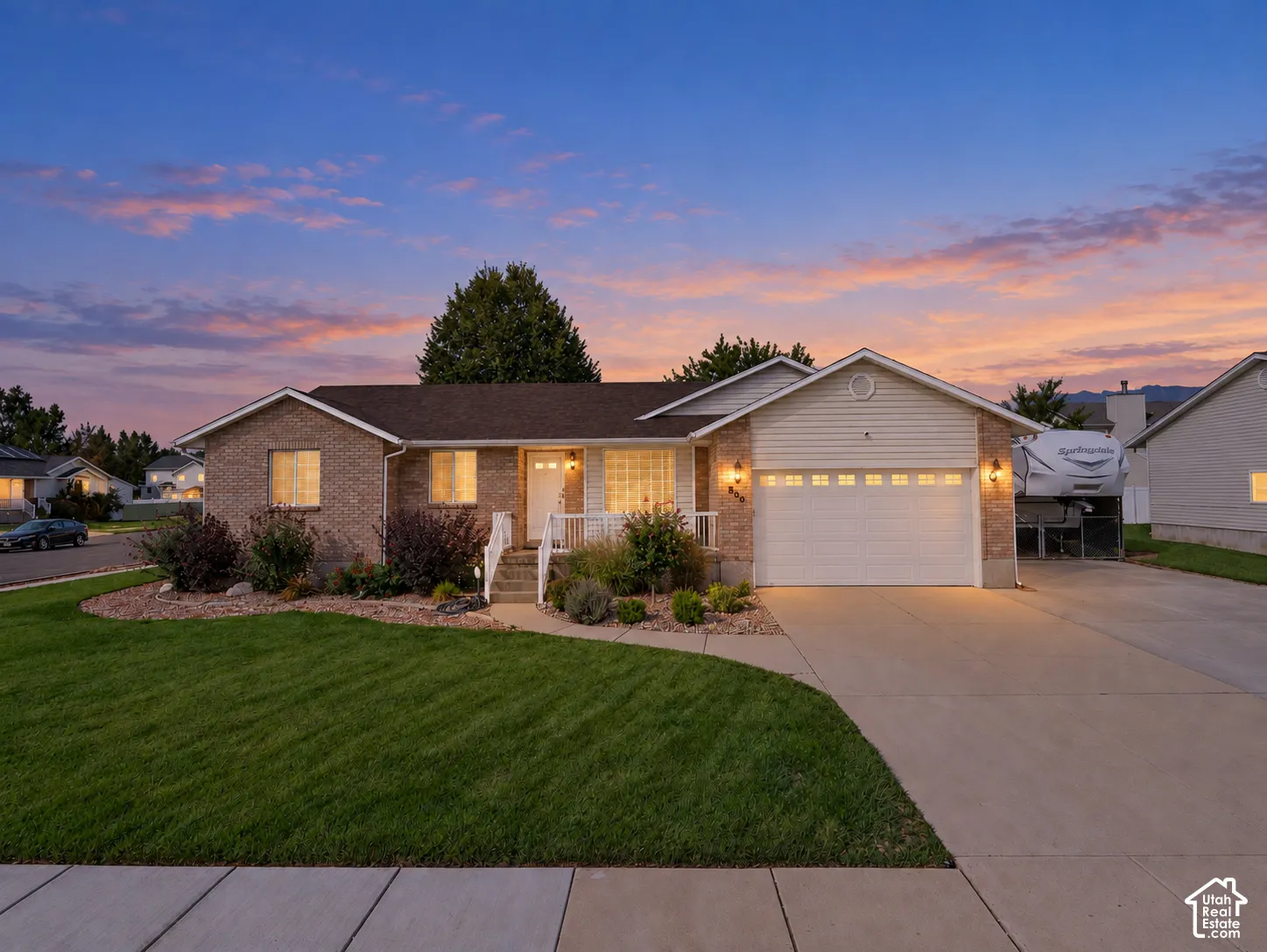 Brick exterior with white trim, attached two-car garage, concrete driveway, and a landscaped front yard