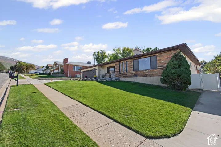 Exterior featuring stone accent siding, a concrete driveway, a concrete sidewalk, and a manicured lawn
