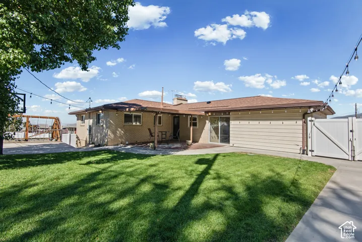 Expansive backyard featuring a concrete patio, a green lawn, and a white fence with a gate