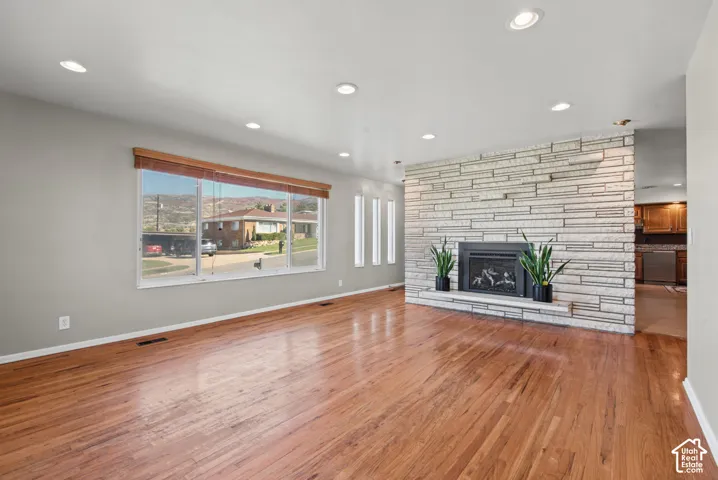 Hardwood flooring, recessed lighting, expansive window, stone-clad fireplace with mantel, and built-in fireplace insert