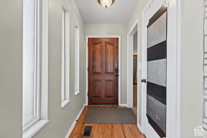 Hardwood flooring, paneled entry door, multiple windows, overhead lighting, and a barn door