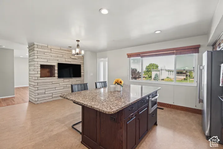 Kitchen island with a granite countertop and integrated oven, stainless steel refrigerator, and wood-finish flooring