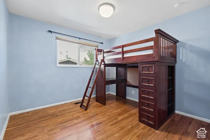 Wood-finish flooring with a built-in loft bed featuring a desk, drawers, and shelving