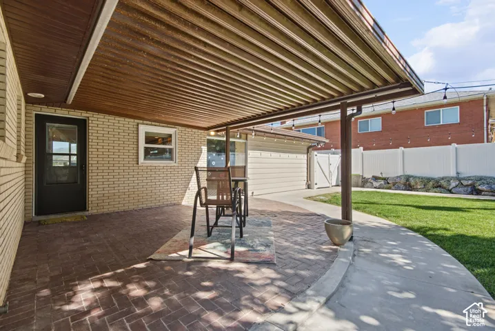 Covered patio with brick-finish flooring, light brick exterior, and a manicured lawn