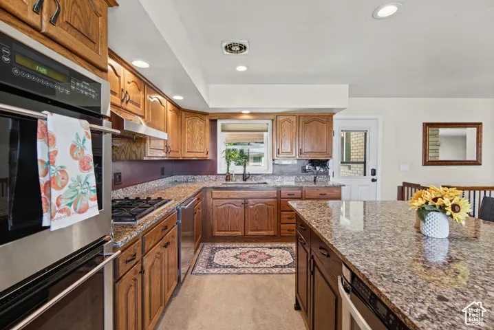 Integrated stainless steel oven and microwave, gas cooktop, wood cabinetry, stone countertops, and recessed lighting