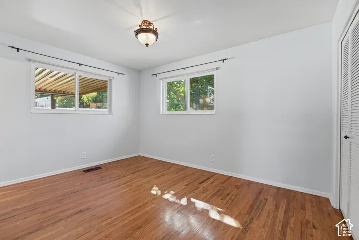 Hardwood flooring, white walls, multiple windows, built-in closet with louvered doors, and a ceiling-mounted light fixture