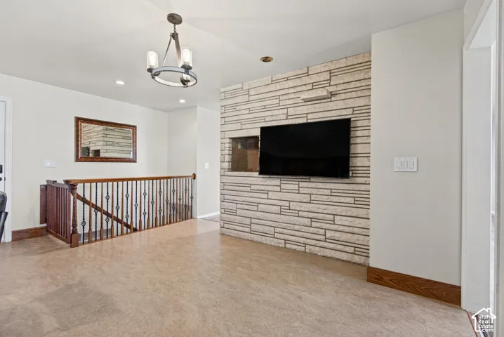 Staircase with wood newel posts and wrought iron balusters, stone-clad accent wall, recessed lighting, and a chandelier with glass shades