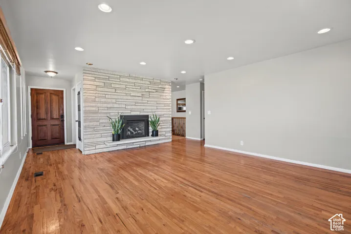 Hardwood flooring throughout, recessed lighting, fireplace with stone surround, and paneled entry door
