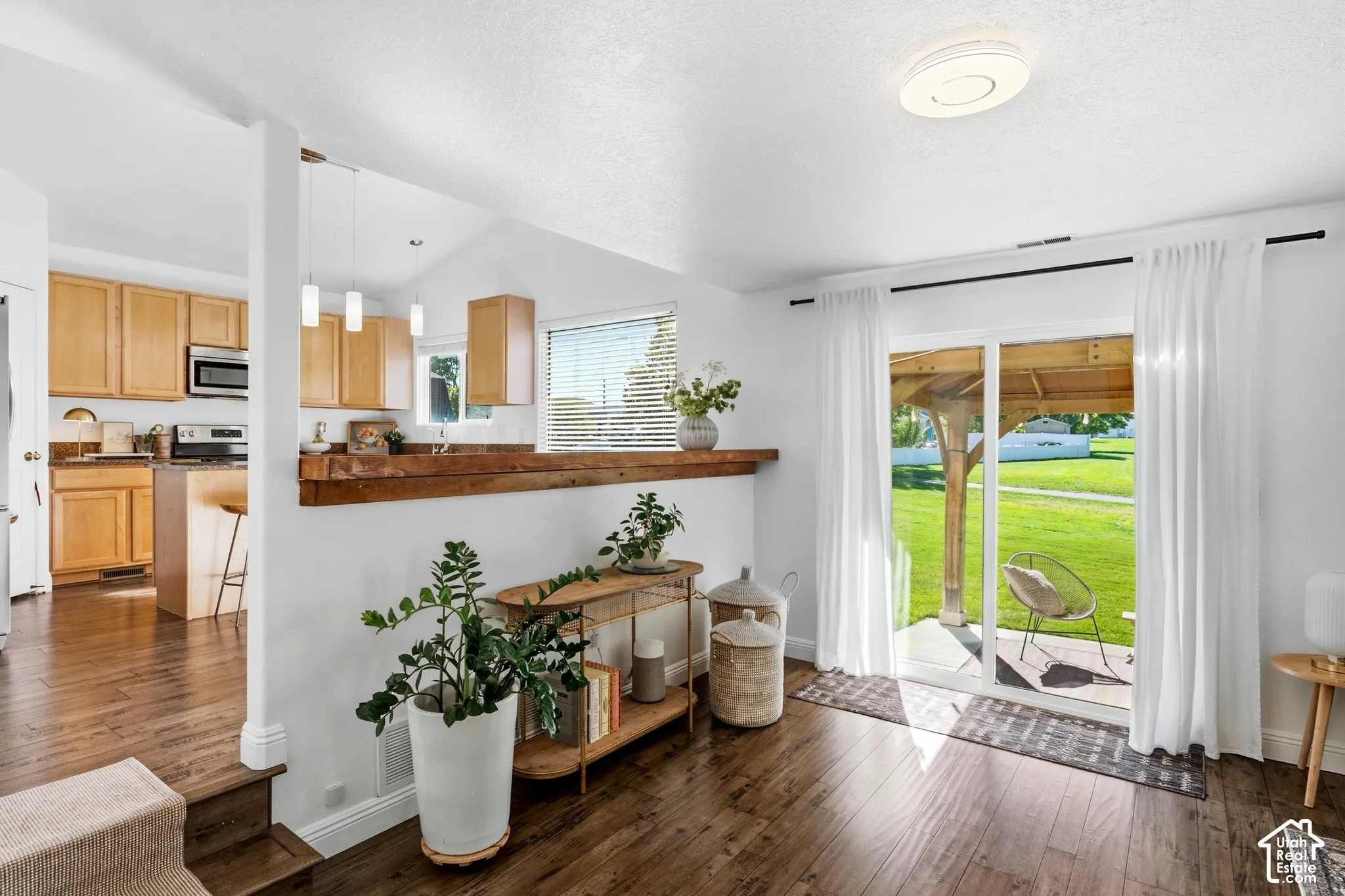 Wood-finish flooring throughout, with a kitchen featuring light wood cabinetry, stainless steel appliances, and pendant lighting