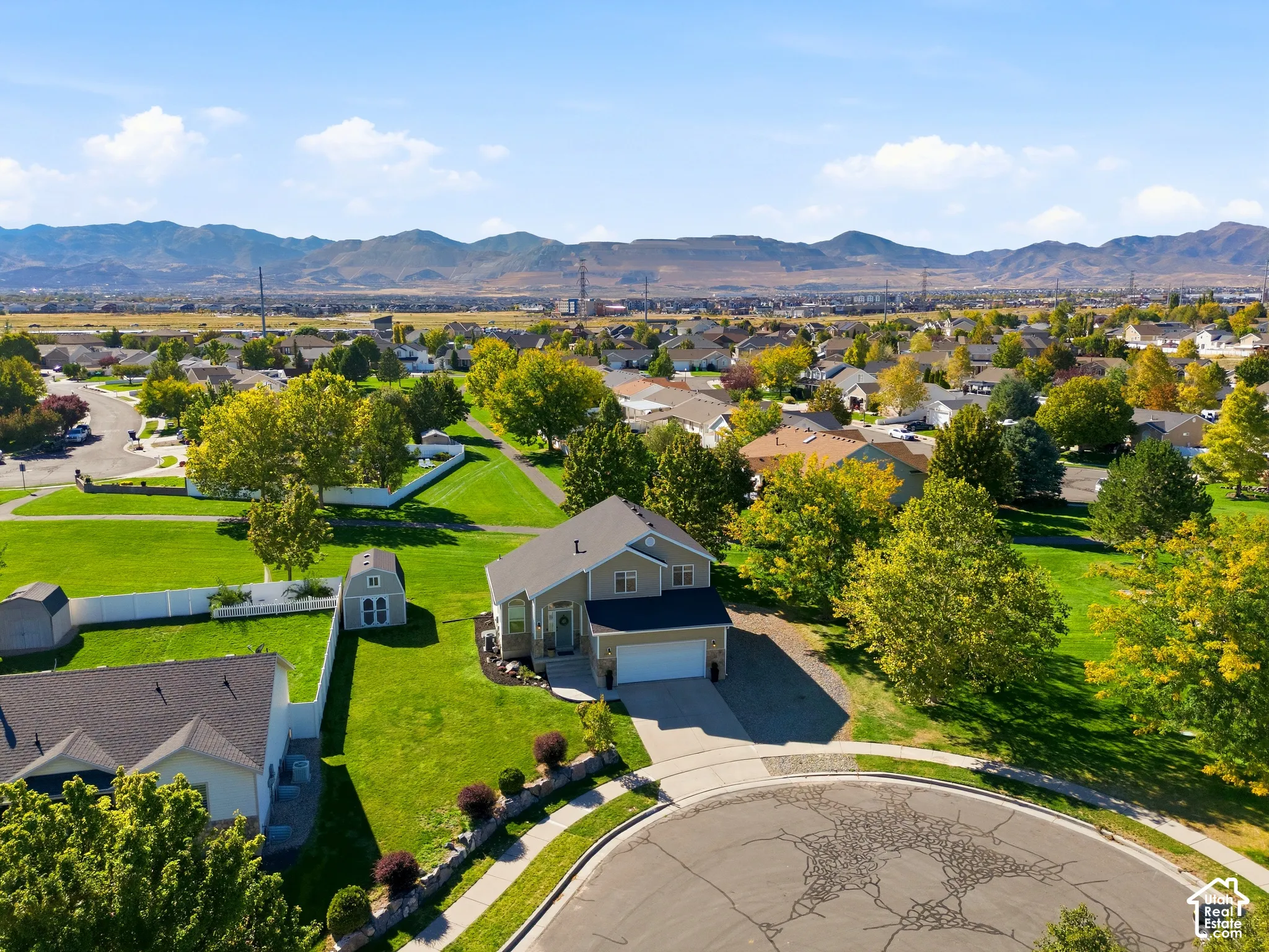 Two-story home with a two-car garage, expansive green lawn, and mature trees