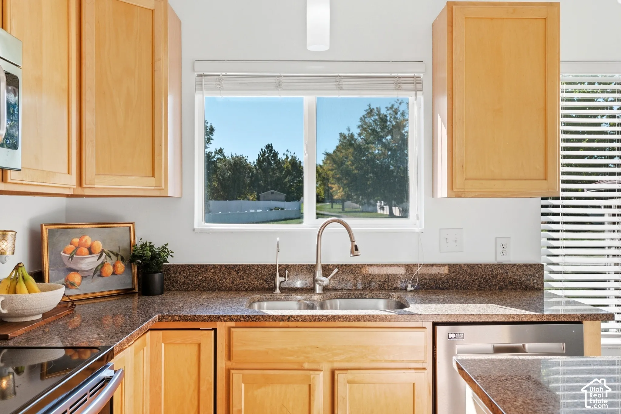 Wood-finish cabinetry, stainless steel sink with gooseneck faucet, brown granite countertops, and built-in dishwasher