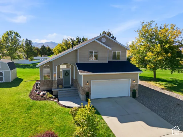 Two-story residence featuring light tan siding and dark roof, stone facade accents, an arched front entry, and an attached two-car garage