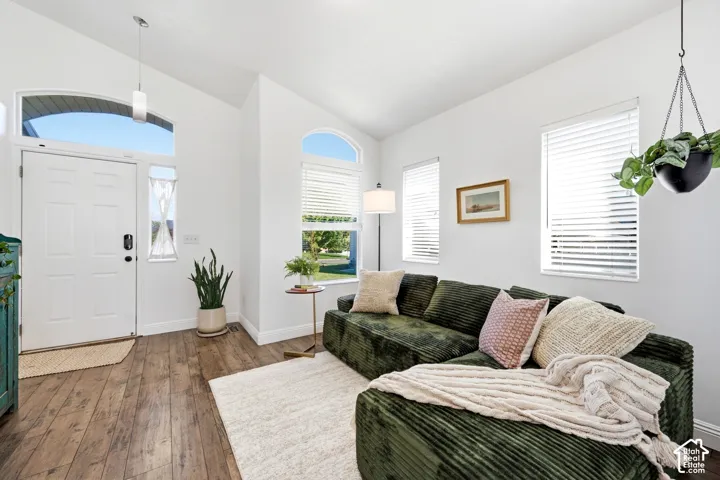 Vaulted ceilings, wood-finish flooring, white paneled door with arched transom window, multiple windows with blinds, and recessed lighting