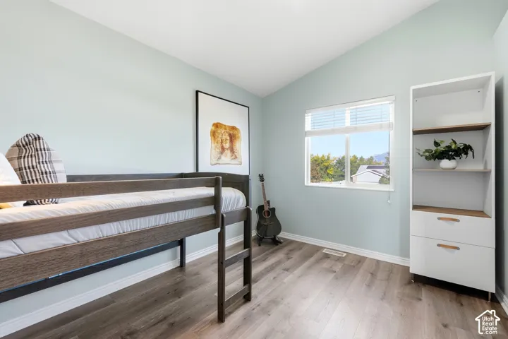 Sloped ceiling room featuring wood-finish flooring, a window with blinds, and a built-in shelving unit with drawers