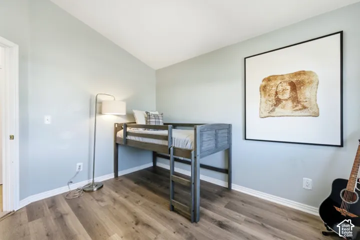 Vaulted ceiling, light-toned wall paint, wood-finish flooring, white trim, and a white interior door