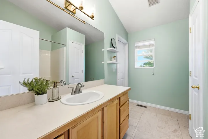 Bathroom featuring a single vanity with wood-finish cabinetry, a large wall-mounted mirror, a window with a blind, and tiled flooring