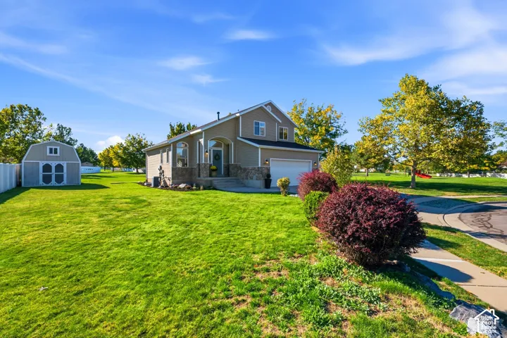 Expansive green lawn with a detached storage shed, a two-story residence, an attached garage, and mature landscaping