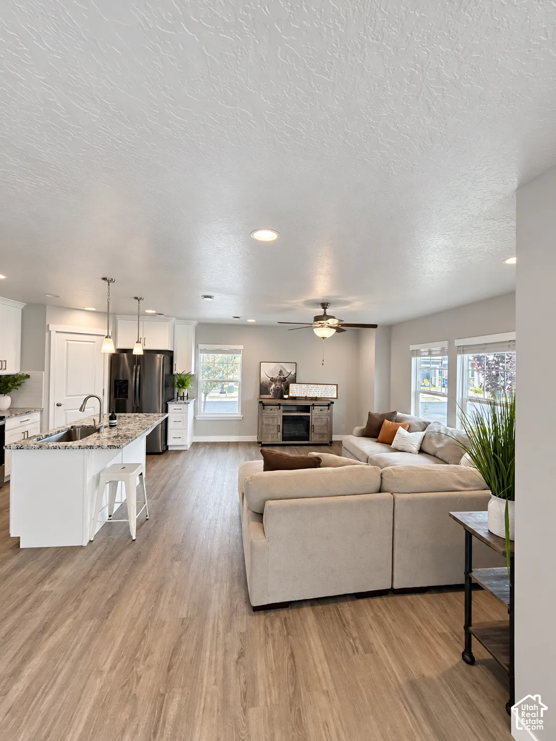 Open-concept living space featuring wood-finish flooring, recessed lighting, kitchen island with stone countertop, dual pendant lights, and ceiling fan