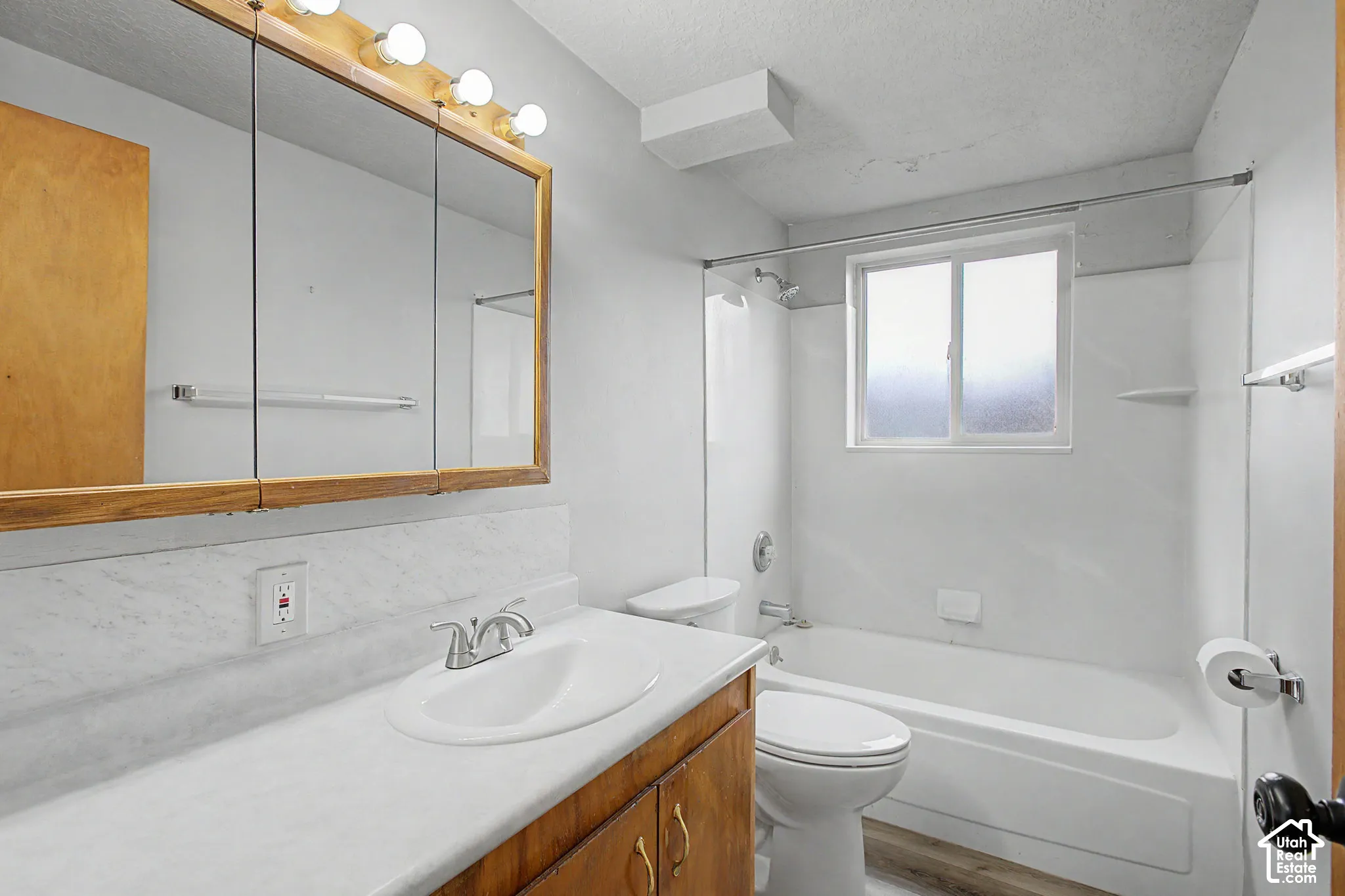 Bathroom featuring a wood-framed medicine cabinet, a white single-sink vanity with a laminate countertop, and a white bathtub with a shower and window