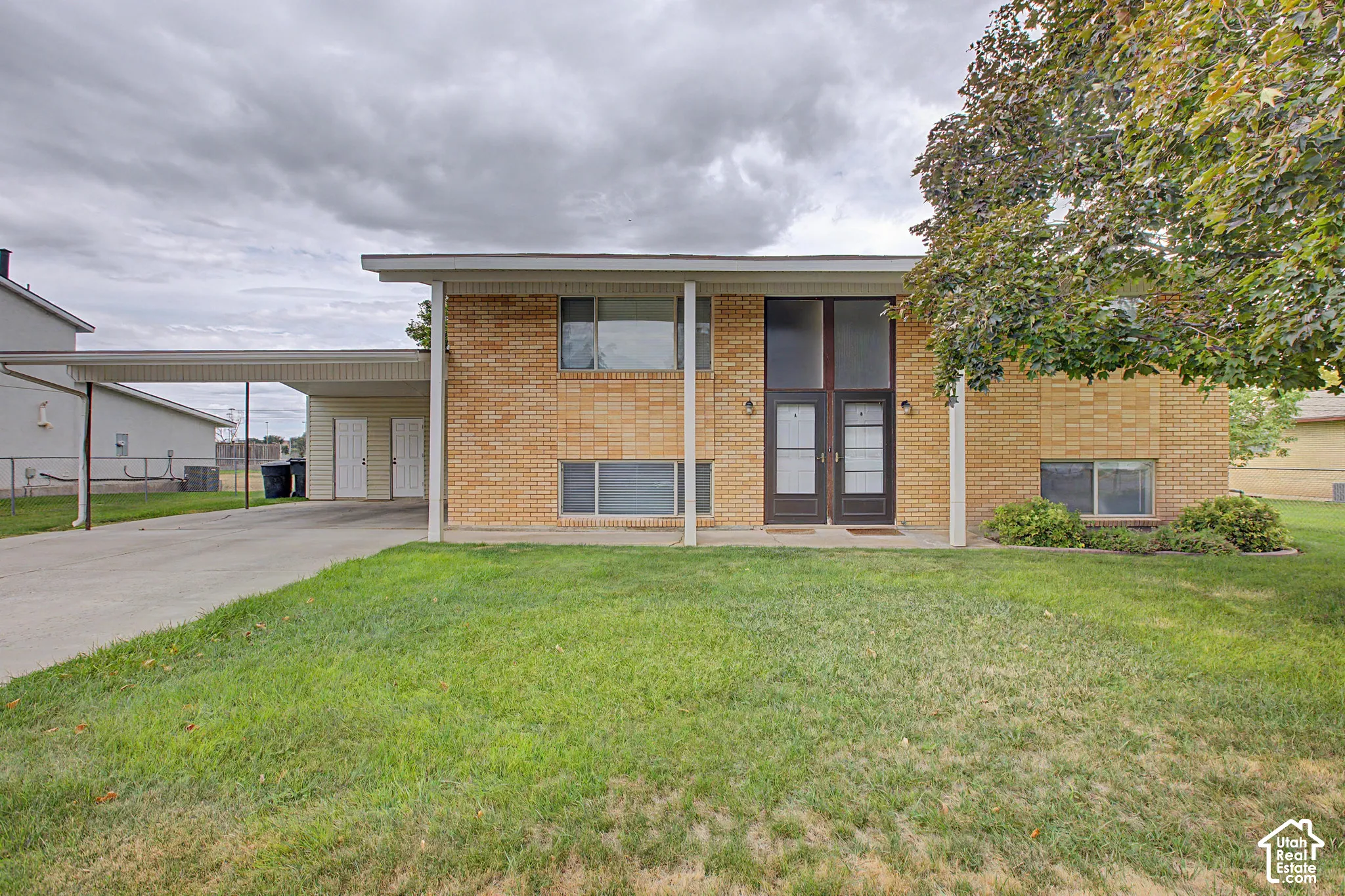 Brick exterior with a covered carport, concrete driveway, and dual entry doors