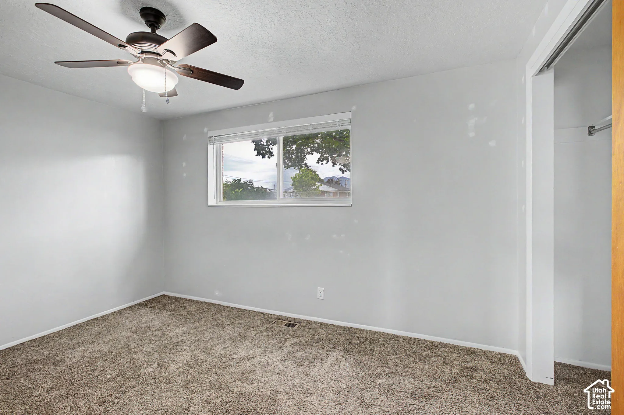Bright bedroom with neutral carpeting, ceiling fan with integrated lighting, and large casement window providing natural light