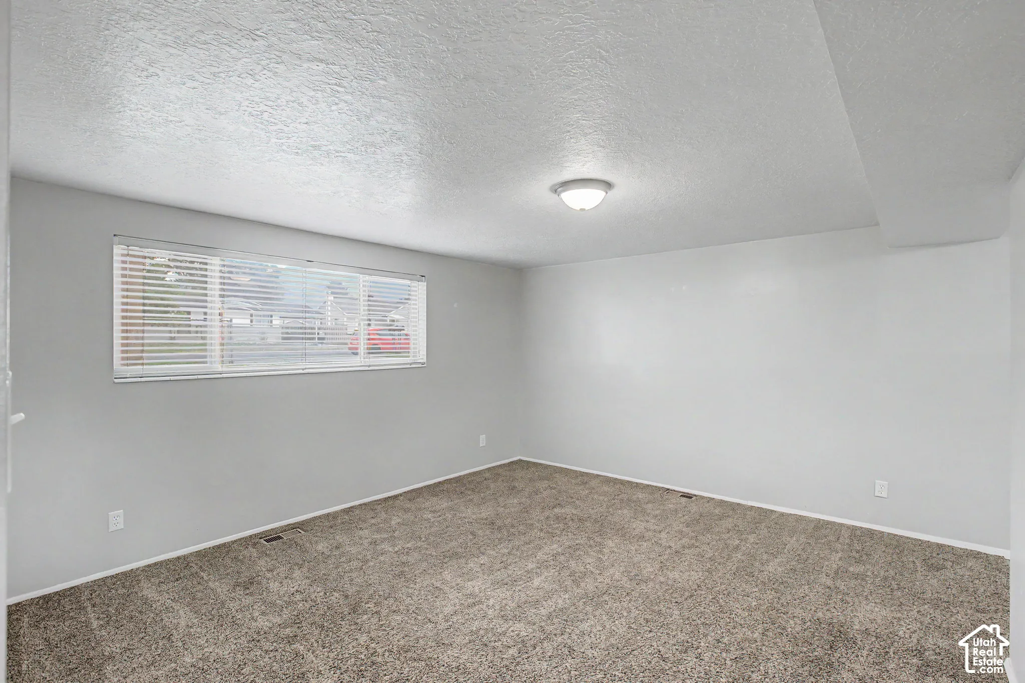 Spacious carpeted bedroom featuring neutral wall finishes, abundant natural light from a horizontal window, recessed ceiling lighting, and clean architectural lines throughout