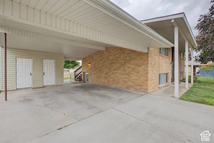 Brick exterior featuring a covered carport, concrete driveway, and two exterior storage doors